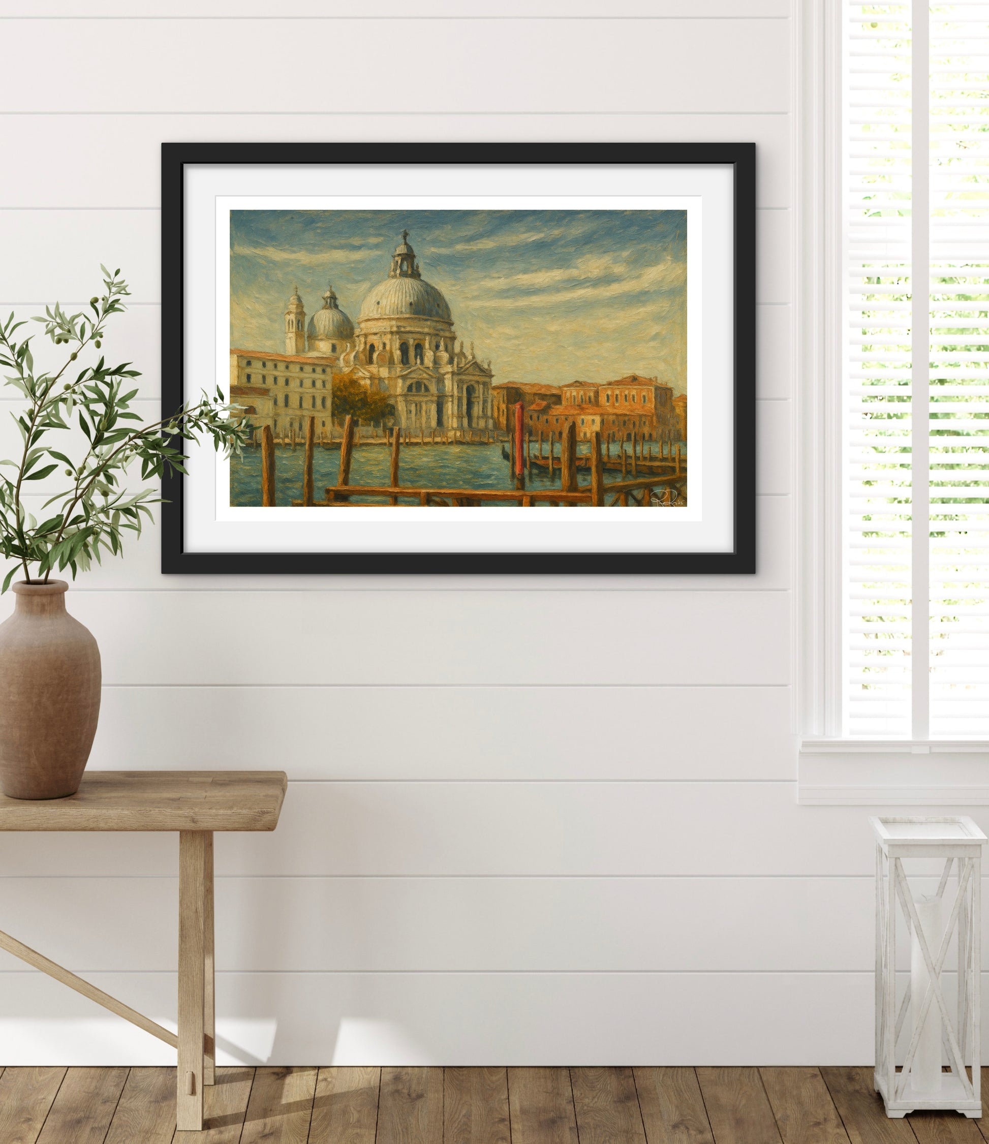 Framed artwork of a cityscape on a white wall with a wooden table and plant.
