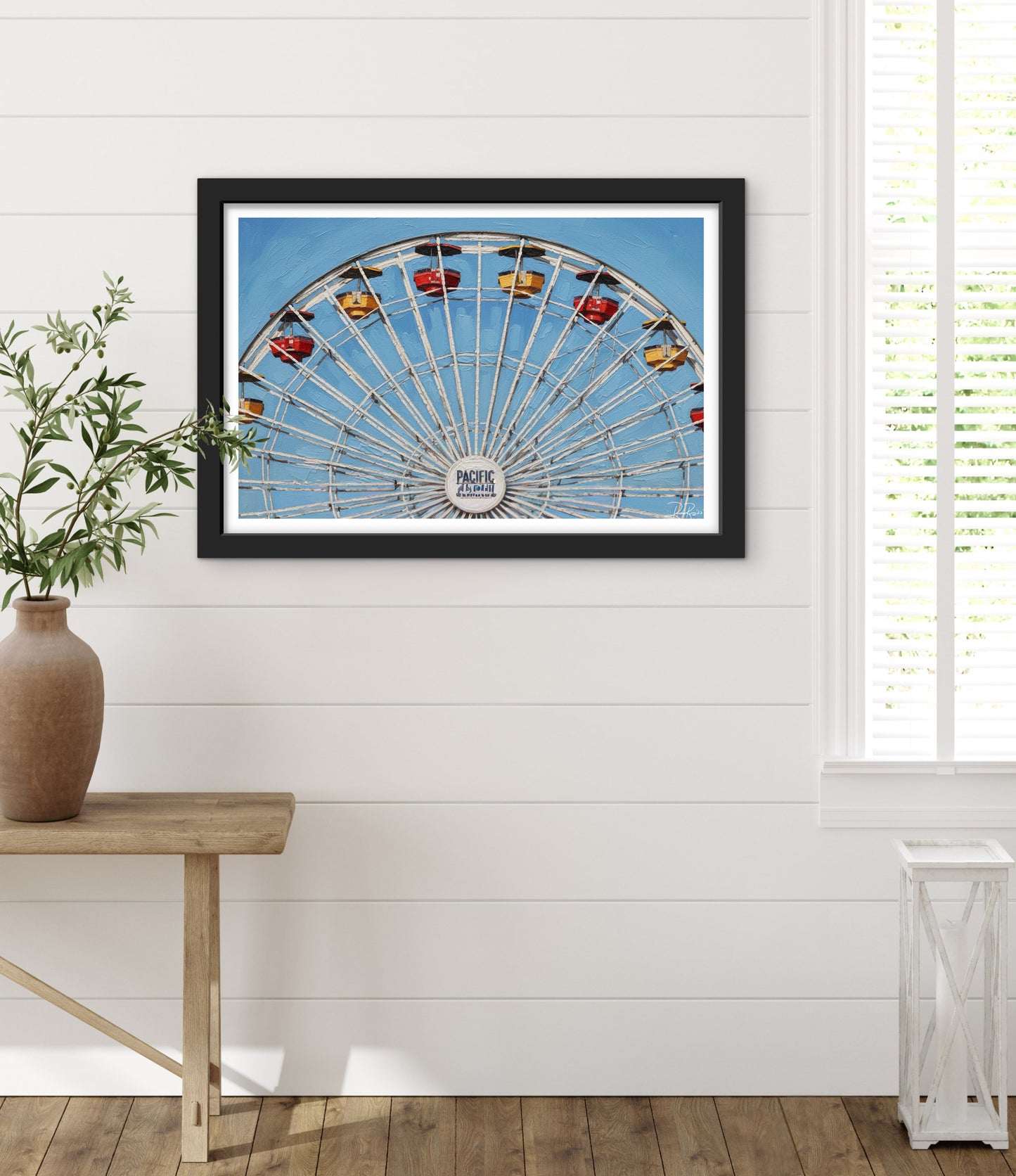 Framed picture of a Ferris wheel on a white wall with a plant and table in the foreground.